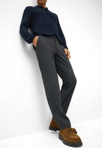 Marineblauwe langemouwen shirt, grijs met patroon broek en bruine suède schoenen. Het shirt heeft een kraag; de broek heeft zijzakken en een ontspannen pasvorm.