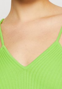 Zielony prążkowany top z dekoltem w serek i cienkimi ramiączkami. Tkanina wydaje się miękka i teksturowana, podkreślając pionowe linie wzoru.