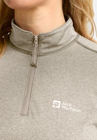 Ripresa ravvicinata di una persona che indossa una felpa grigia Jack Wolfskin con zip, con logo sul petto e dettagli visibili del colletto e della cerniera.