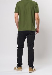 Camiseta verde oliva de cuello redondo, combinada con jeans negros ajustados y zapatillas beige con acentos oscuros y suela texturizada.