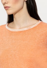 Light orange sweater with a soft, textured fabric. Features a crew neck and a contrasting white trim around the neckline.
