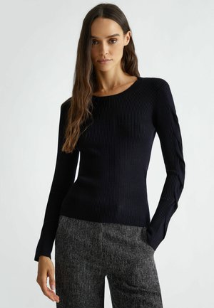 Maglietta nera a maniche lunghe con collo rotondo e dettagli testurizzati sulle maniche, abbinata a pantaloni grigi con texture.
