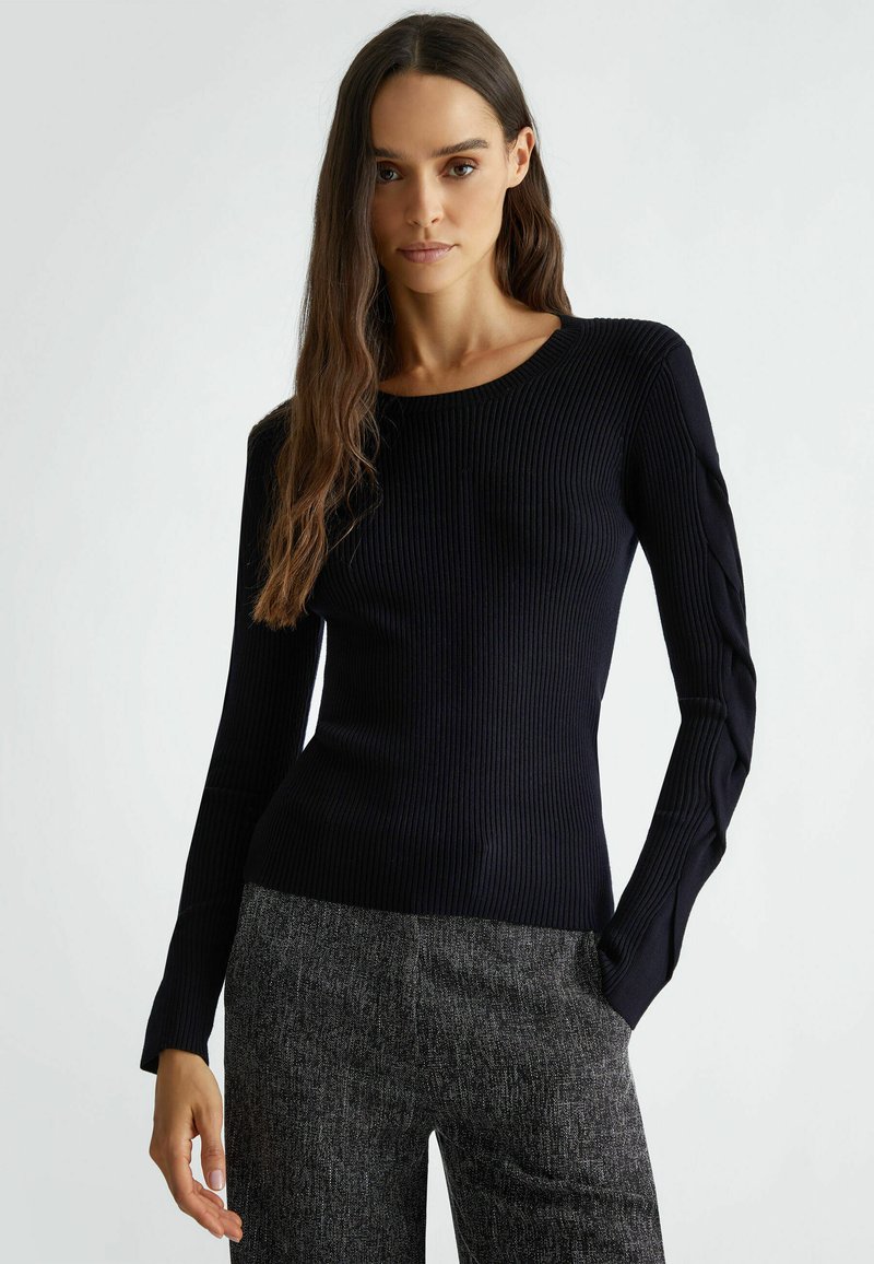 Maglietta nera a maniche lunghe con collo rotondo e dettagli testurizzati sulle maniche, abbinata a pantaloni grigi con texture.