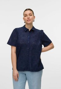 Camicia blu navy a maniche corte con motivo a occhiello floreale, apertura frontale con bottoni e maniche leggermente a sbuffo. Abbinala a denim azzurro chiaro.
