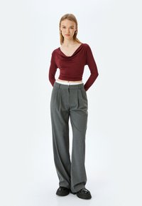 Bourgondische langemouwtop met een gedrapeerde halslijn, gecombineerd met hoge grijze geplooide broek en stevige zwarte schoenen.