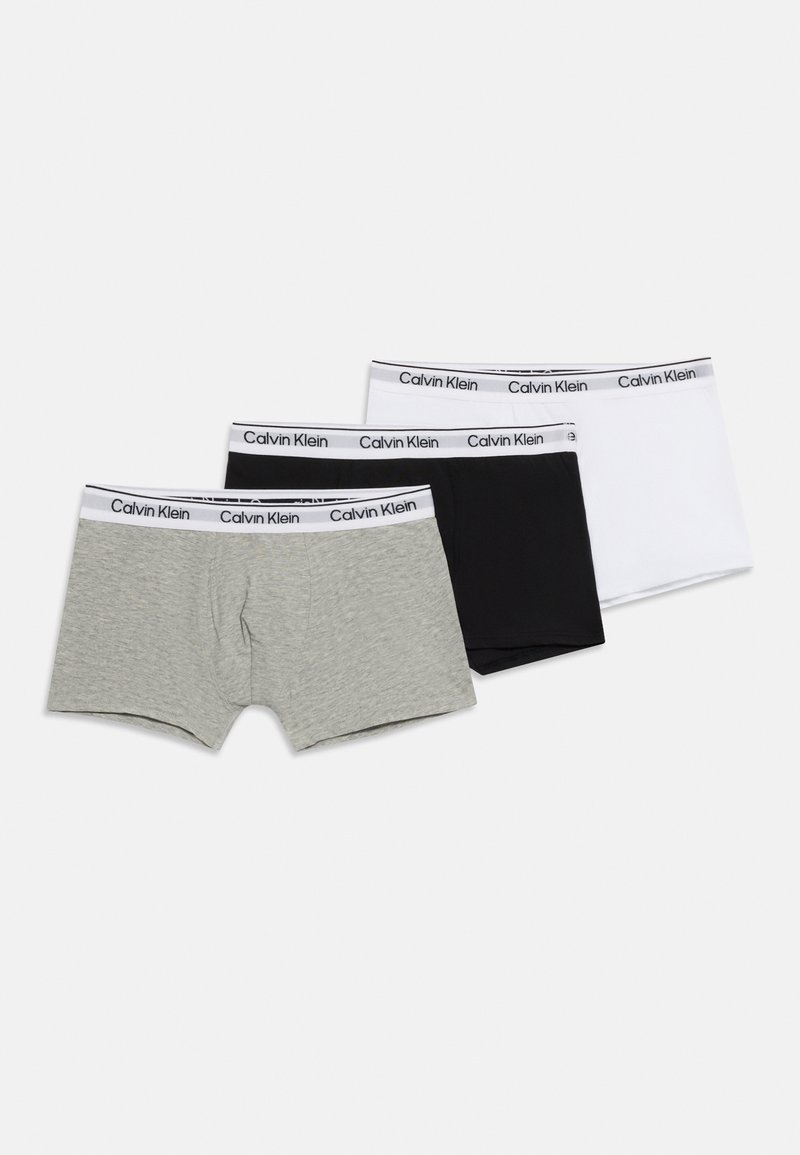 Τρία ζευγάρια ανδρικά μπόξερ Calvin Klein σε γκρι, μαύρο και λευκό με λογότυπα στη μέση, τοποθετημένα επίπεδα σε λευκή επιφάνεια.