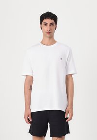 White cotton t-shirt with short sleeves, round neck, and small black logo on the left chest. Paired with black shorts.