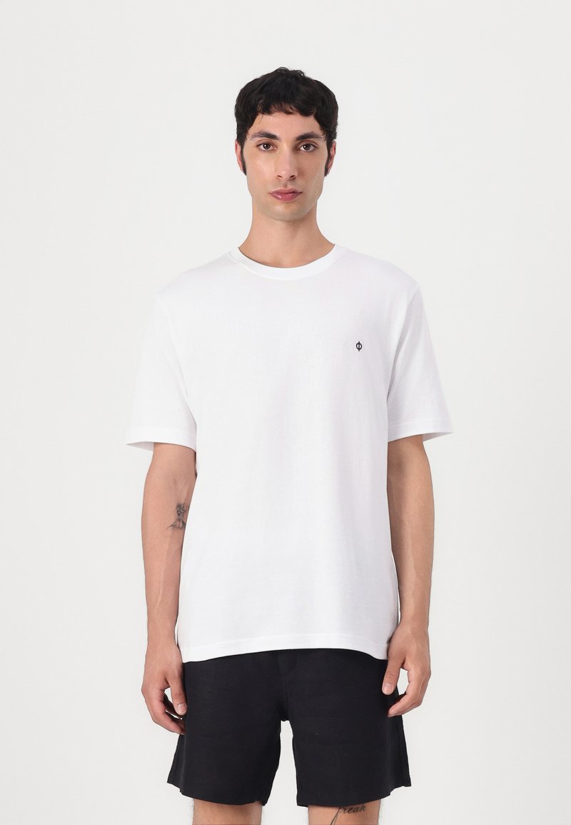 White cotton t-shirt with short sleeves, round neck, and small black logo on the left chest. Paired with black shorts.