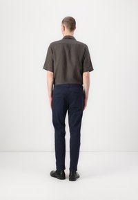 Krátky rukáv, tmavosivá košeľa so jednoduchým límcom, v kombinácii s námořníckymi slim-fit nohavicami a čiernymi topánkami, ktoré predvádzajú čistý, minimalistický dizajn.