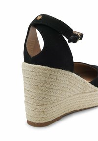 Espadrille compensée en daim noir avec bride cheville et semelle en jute tressé, vue en angle montrant les détails arrière et latéraux.
