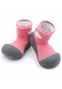 Zapatos de tela rosa claro tipo slip-on con una suela de goma gris y un tobillo acanalado. El diseño incluye un acento juguetón en la parte superior.