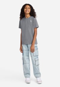 Grå kortærmet t-shirt med lille grafik, parret med lyseblå cargo-bukser med flere lommer og en afslappet pasform. Hvide sneakers.