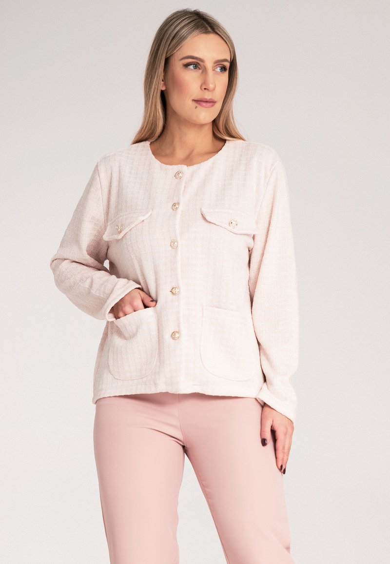 Jasnoróżowa, tkana kurtka z przednimi kieszeniami i okrągłym dekoltem. Posiada cztery guziki i długie rękawy, z teksturowanym materiałem na całej powierzchni.