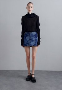 Črn rebrast dolgrokavni top, denim mini krilo s patchworkom v odtenkih modre barve in črne masivne čevlje s gležnjarji.