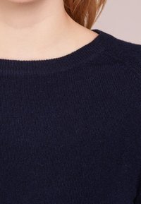 Mörkblå stickad tröja med rund halsringning och fin textur, med en slät finish och raglanärmar.