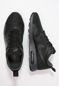 Ett par svarta Nike Air Max sneakers, en som visar övervy med snörning, den andra i sidovy som visar luftkuddsålen.