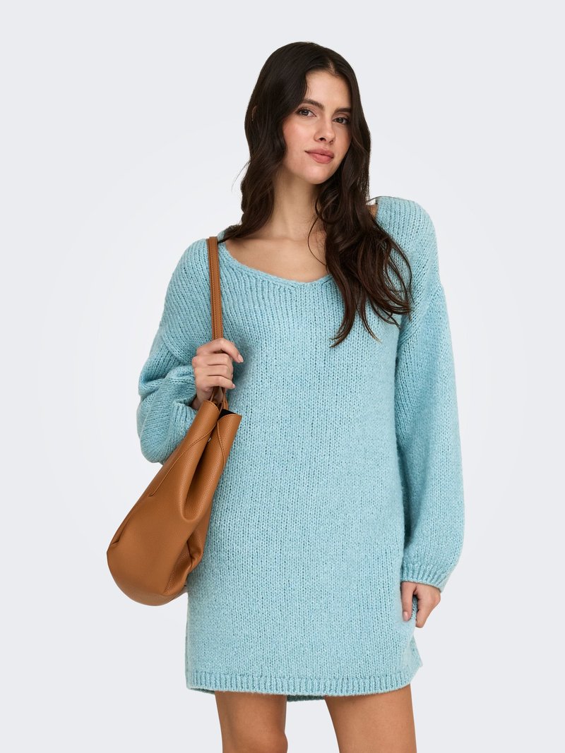 Light blue, oversized knitted sweater dress with long sleeves and a wide neckline. Model holds a brown, textured shoulder bag.