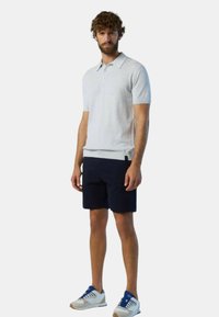 Polo a maniche corte grigio chiaro con colletto, abbinato a pantaloni corti blu navy e sneakers bianche con dettagli blu.
