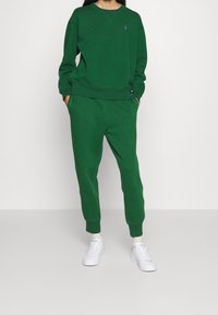 Grön bomullströja med rund halsringning och ribbade ärmslut, matchad med gröna sweatpants som har sidofickor och nederkant med mudd.