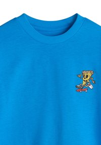 Blue t-shirt featuring a cartoon pizza character on a skateboard. Made from cotton blend material with a round neckline and short sleeves.