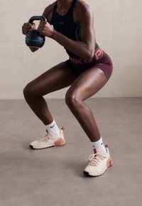 Tenue de sport composée d'un débardeur noir et d'un short bordeaux. Comprend des baskets beiges avec des semelles noires et un talon dégradé, tenant un kettlebell bleu.
