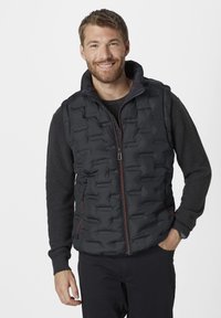 Schwarze Steppweste mit einem gesteppten Design, Reißverschluss vorne und Seitentaschen. Getragen über einem dunklen Pullover mit hohem Kragen und strukturierten Ärmeln.