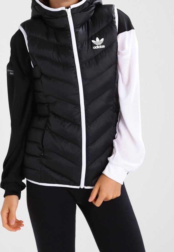 Černobílá péřová vesta se vzorem ve tvaru šipky, s kapucí, předním zipem a třemi bílými pruhy na rukávech. Na hrudi logo Adidas.