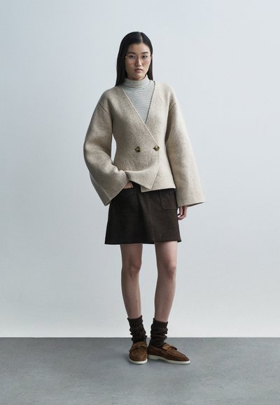 Kremasti oversized vuneni blejzer s dvostrukim kopčama, nošen preko prugastog rolka. Uparen s tamnosmeđom suknjom od brušene kože i smeđim cipelama.