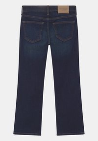 Granatowe dżinsy o prostym kroju, z dwiema tylnymi kieszeniami i skórzaną metką przy pasku. Gładka faktura i staranne wykończenie.