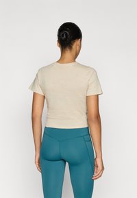 Μπεζ κοντομάνικο μπλουζάκι crop top, σε συνδυασμό με τιρκουάζ κολάν ψηλόμεσο με πλαϊνές ραφές και λεπτομέρεια τσέπης.