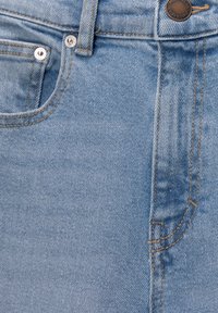 Jean en denim bleu clair avec poches avant visibles, passants pour ceinture, rivets métalliques et fermeture par bouton de marque.