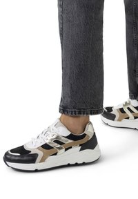 Black, white, and gold sneakers with a textured upper, featuring a chunky white sole and laces, showcasing layered color accents.