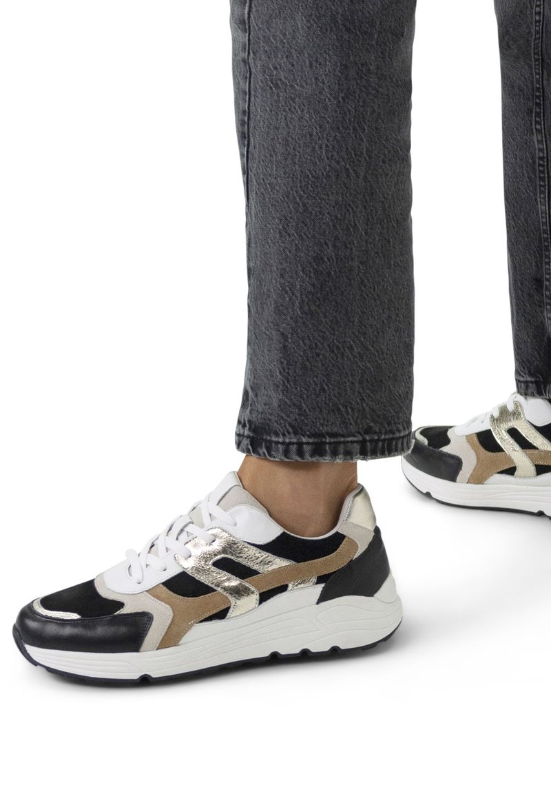 Schwarze, weiße und goldene Sneaker mit einem strukturierten Obermaterial, das eine dicke weiße Sohle und Schnürsenkel aufweist, die farbige Akzente in mehreren Schichten zeigen.