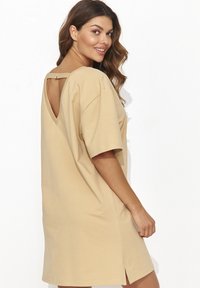 Beżowa, oversize sukienka T-shirt, krótki rękaw, plecy w kształcie litery V z detalem z klamrą, boczne rozcięcia, miękki materiał bawełniany, luźny krój.