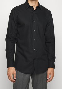 Svart långärmad skjorta i mjukt material med klassisk krage, knappstängning fram och subtil lyster. Knapparna är mörka och i ton med skjortan.