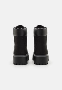 Sorte ankelboots med en kombinasjon av glatt lær og semsket skinn, med en grov gummisåle og rund krage. Synlige sømdetaljer.