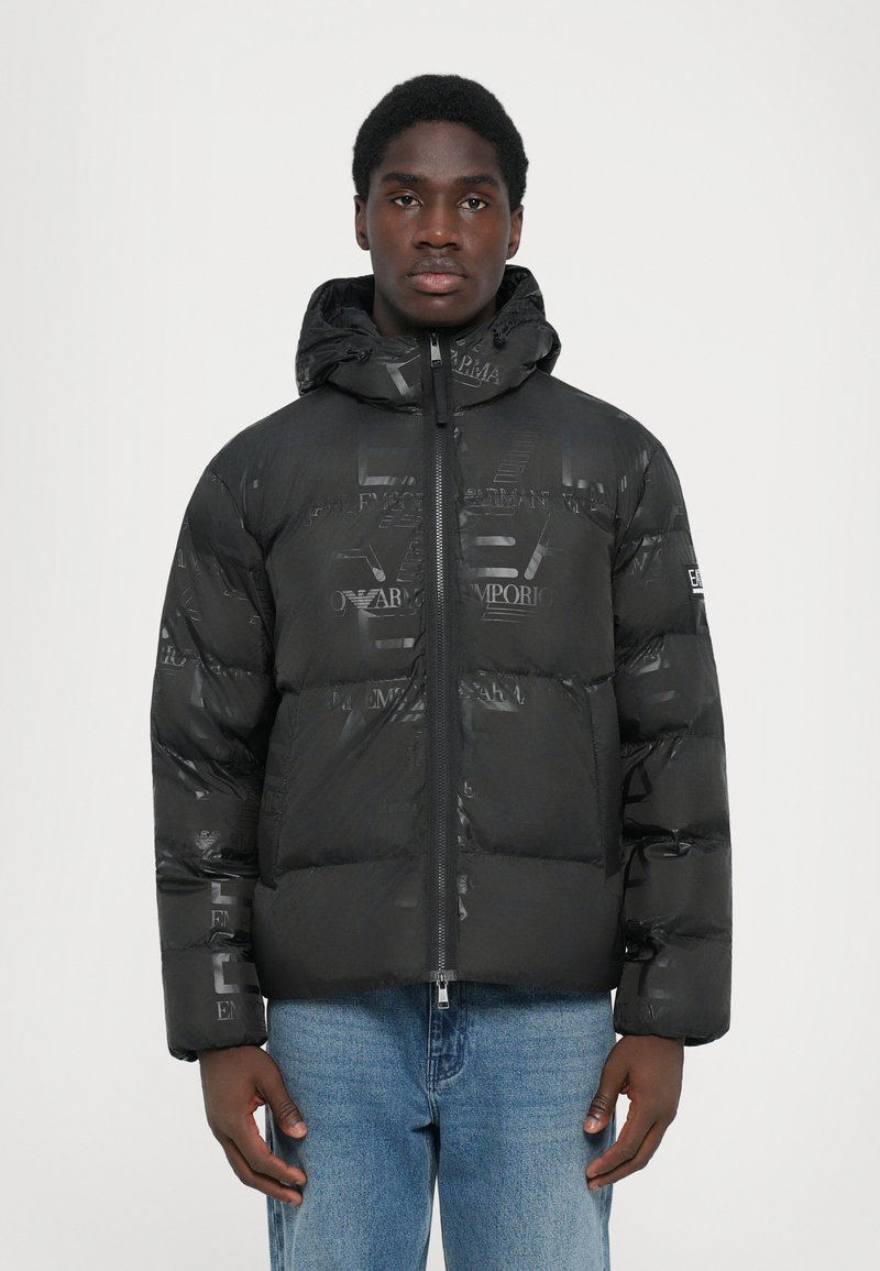 Schwarze Steppjacke mit glänzender Oberfläche, ausgestattet mit einem Reißverschluss vorne, Kapuze und geprägten Logo-Mustern. Strukturierte, isolierte Ausführung.
