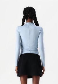 Maglione azzurro chiaro a maniche lunghe con scollatura alta, caratterizzato da tessuto arricciato sul retro, abbinato a una gonna nera. Texture morbida in generale.