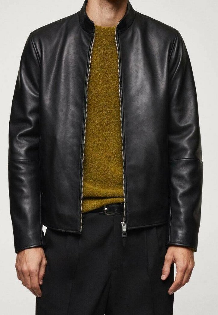 Giacca di pelle nera con colletto rotondo e zip frontale. Il modello indossa un maglione giallo-mustard sotto. Tessuto liscio, design aderente.