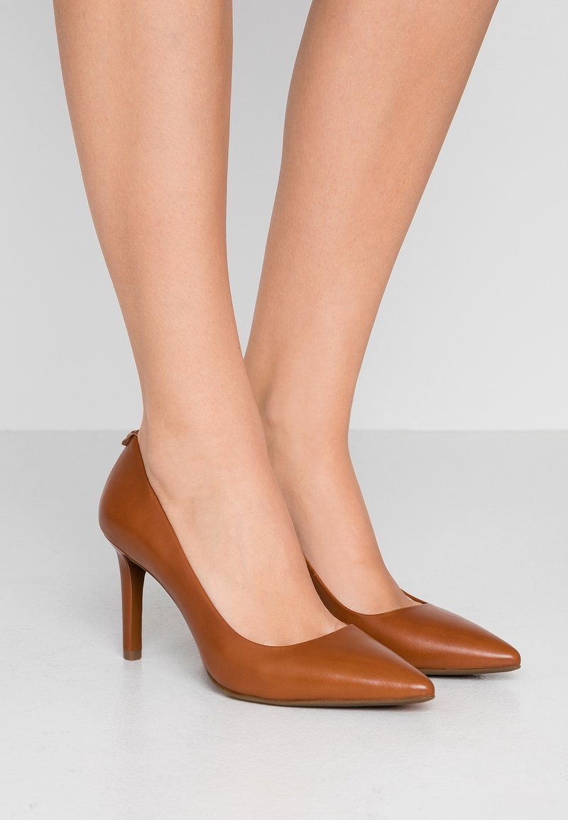 Escarpins en cuir marron à bout pointu et design épuré. Les chaussures présentent une discrète découpe à l'arrière et un talon aiguille.