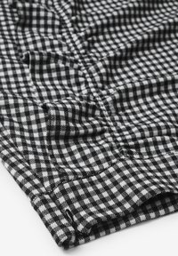 Tessuto a scacchi bianco e nero con bordo arricciato, che mostra una superficie texture e un motivo strettamente intrecciato, piegato con cura.