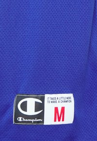 Modrá síťovina s texturovaným povrchem; obsahuje černobílou nášivku s logem a červeným "M" a textem, který říká: "Je třeba trošku víc, abychom vytvořili šampiona."