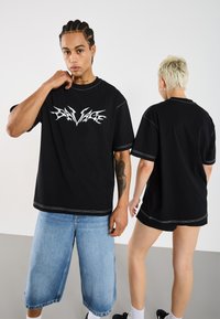 Black oversized t-shirt with white "Savage" graphic on the front, contrast stitching, paired with light blue denim shorts.
