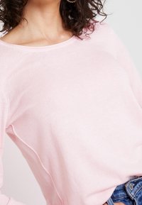 Suéter largo de manga larga en color rosa, hecho de un suave tejido de punto, con un escote amplio y una textura sutil, combinado con pantalones cortos de denim.