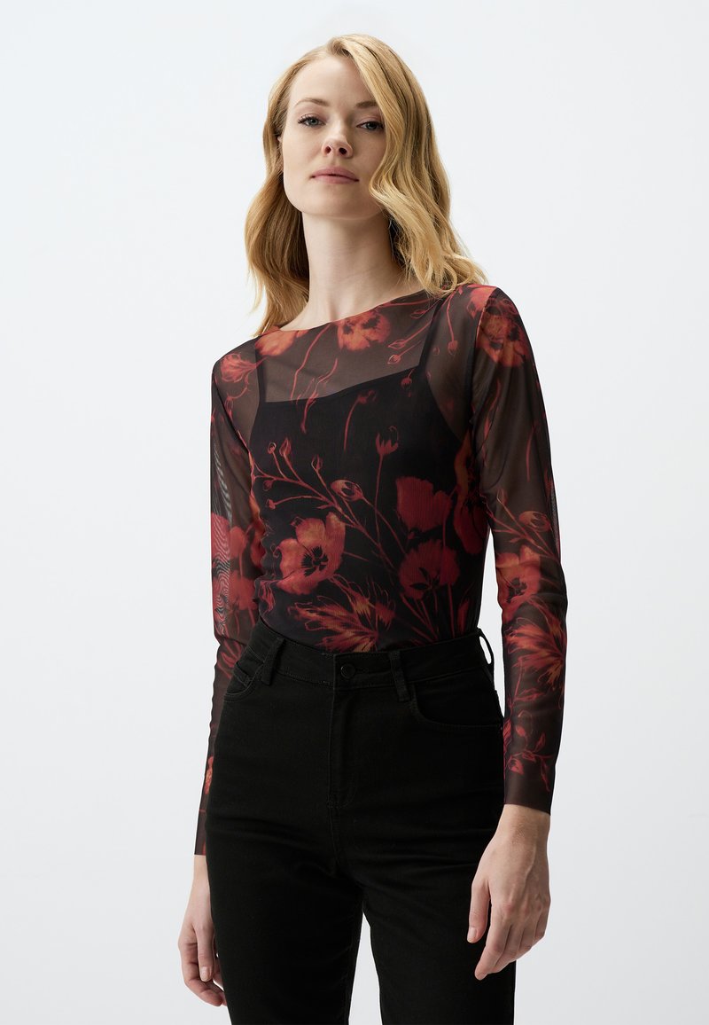 Haut en mesh noir à manches longues avec un motif floral rouge, présentant un col rond. Assorti à un jean noir taille haute.