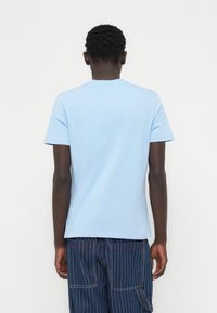 T-shirt en coton bleu clair à col rond et manches courtes, avec une texture lisse. Le tissu semble doux et léger.