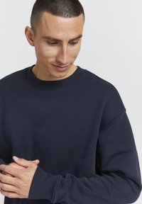 Felpa blu navy con scollo tondo, polsini a costine e vestibilità rilassata. Tessuto liscio con cuciture e dettagli minimi visibili.