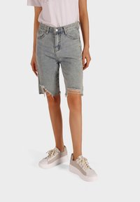 Bermuda shorts in denim chiaro con bordi strappati e orlo sfrangiato. Abbinati a sneaker con plateau beige.