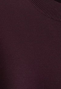 Țesătură tricotată burgundy cu un model texturat, având un decolteu cu dungi. Vedere de apropiere care evidențiază moliciunea materialului și țesătura detaliată.