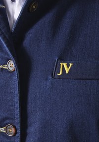 Marineblaue Jeansjacke mit goldgesticktem "JV" auf der linken Brust, mit Knopfverschluss und strukturiertem Stoff.